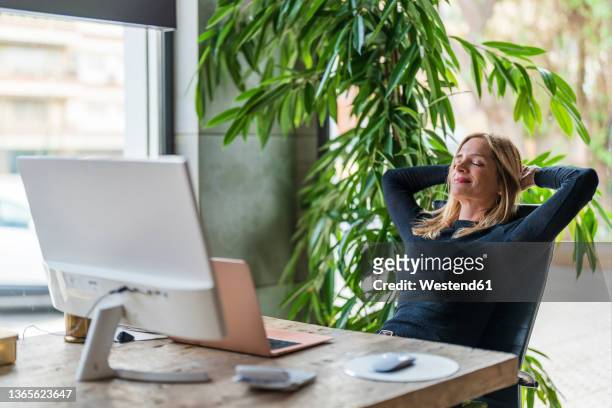 businesswoman relaxing hands behind head at office - cómoda fotografías e imágenes de stock