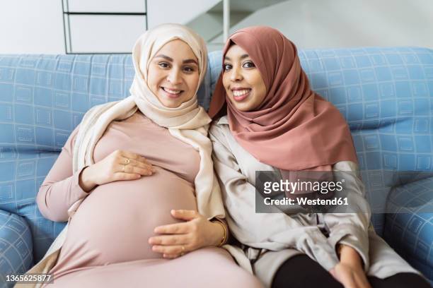 happy friends sitting on sofa at home - pregnant muslim stock pictures, royalty-free photos & images