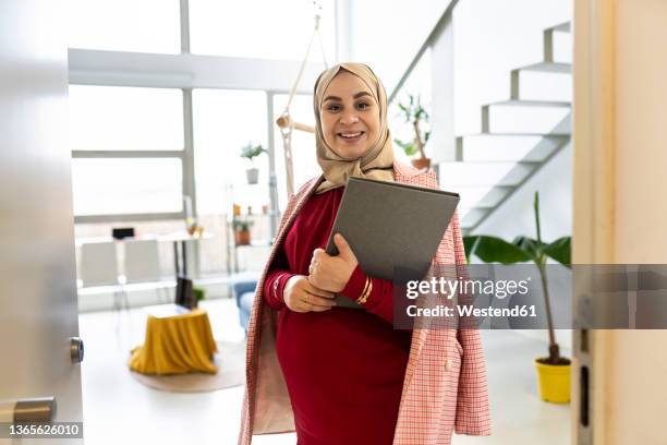 happy pregnant woman with file folder at home - arabische frau kopftuch stock-fotos und bilder