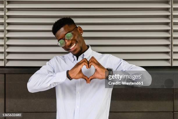 smiling man making heart shape with hands - herz hände stock-fotos und bilder