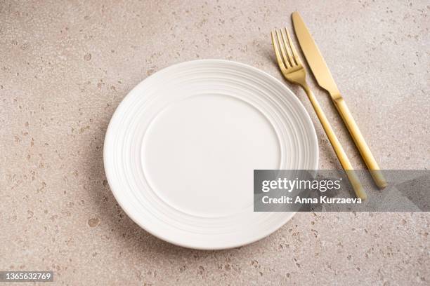 empty white ceramic plate and golden fork and knife on pink concrete background, top view - tisch besteck leer stock-fotos und bilder