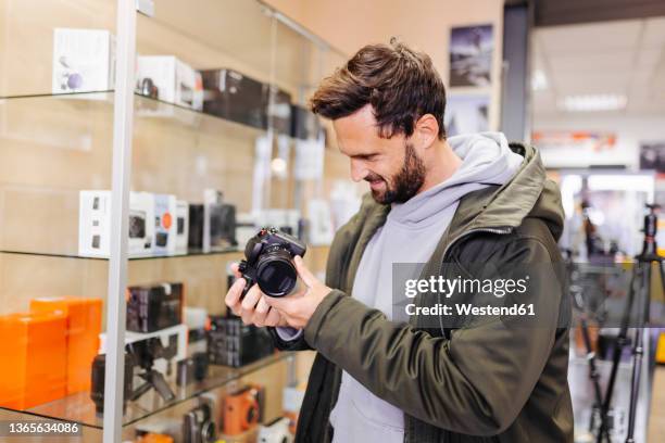 young man examining camera in store - digitale camera stockfoto's en -beelden