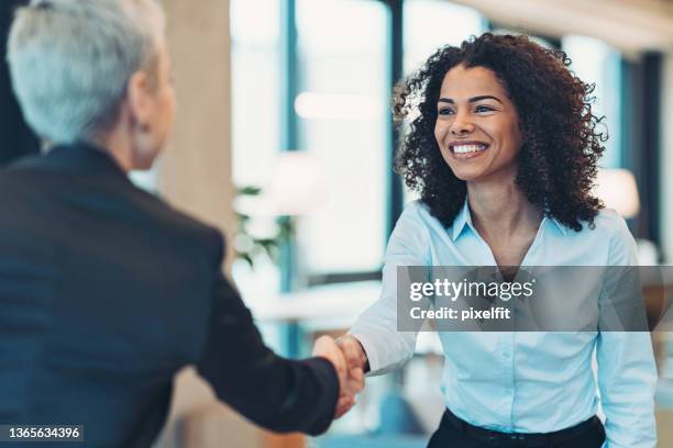 lächelnde geschäftsfrau begrüßt einen kollegen bei einem meeting - african woman happy stock-fotos und bilder