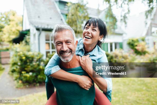 happy man giving piggyback ride to woman in backyard - couple happy outdoors fotografías e imágenes de stock