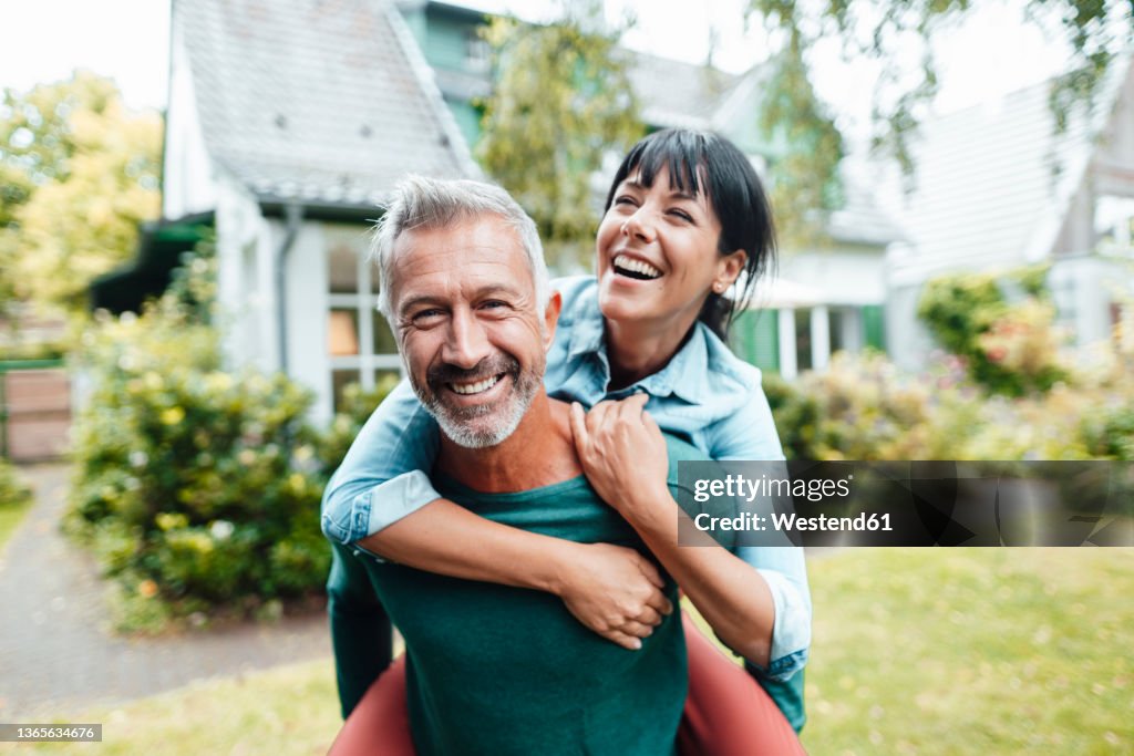 Happy man giving piggyback ride to woman in backyard