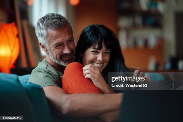 happy mature couple using tablet pc in living room - 45 couple stockfoto's en -beelden