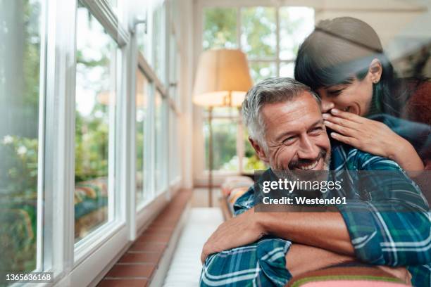 happy woman whispering in man's ear at home - whispering stock pictures, royalty-free photos & images