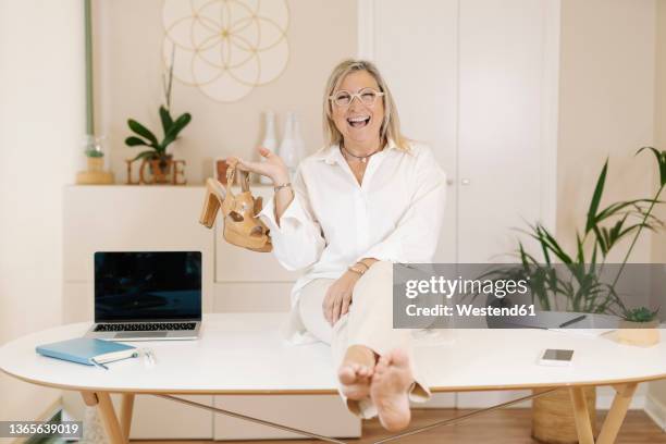 cheerful businesswoman sitting with high heels on desk at workplace - businesswoman barefoot stock-fotos und bilder