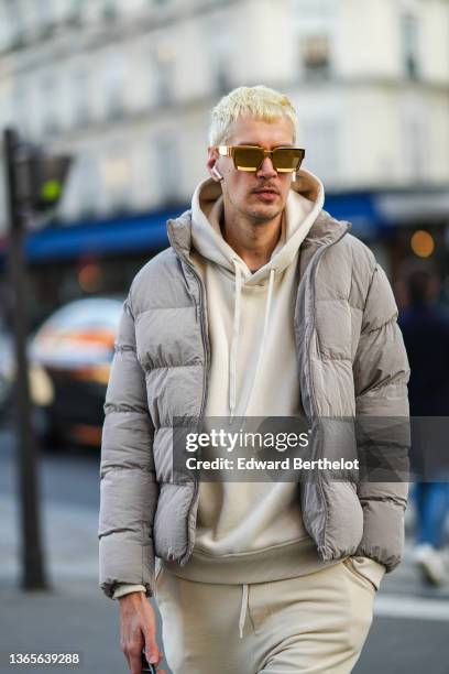 Guest wears gold sunglasses, a pale yellow hoodie sweater, matching pale yellow sport pants, a gray high neck puffer jacket, outside the Bluemarble...