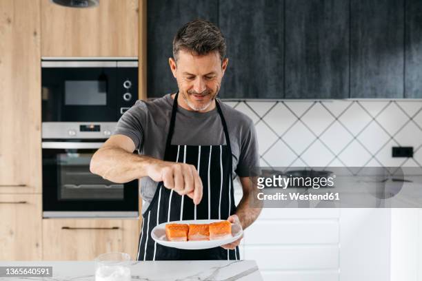 smiling man seasoning raw fish in kitchen at home - cooking fish stock pictures, royalty-free photos & images