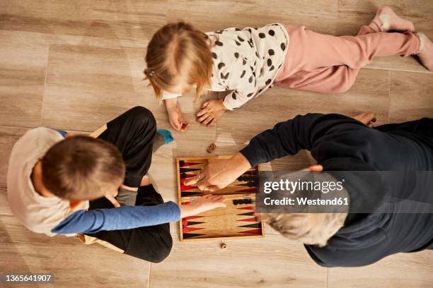 grandfather teaching backgammon to grandchildren lying down at home - game night stock pictures, royalty-free photos & images