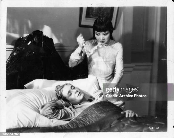 Anna May Wong about to stab a sleeping man in a scene from the film 'Daughter Of The Dragon', 1931.