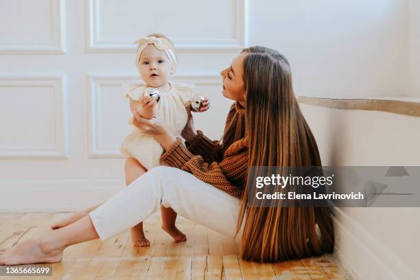 beautiful young woman plays with a little girl. mother and child. motherhood and mother's day concept. side view of a lady playing with a one-year-old baby - fashionable mom stock pictures, royalty-free photos & images