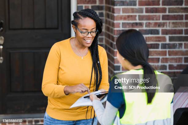 smiling woman signs for package on digital tablet - signing tablet stock pictures, royalty-free photos & images