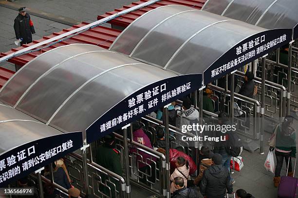 Chinese people walk with their luggage at the entrance of the check-in kiosks for real-name tickets as a policeman looks at Beijing West Railway...