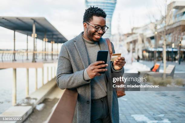 afro american businessman using smart phone on city street - charging phone stock pictures, royalty-free photos & images