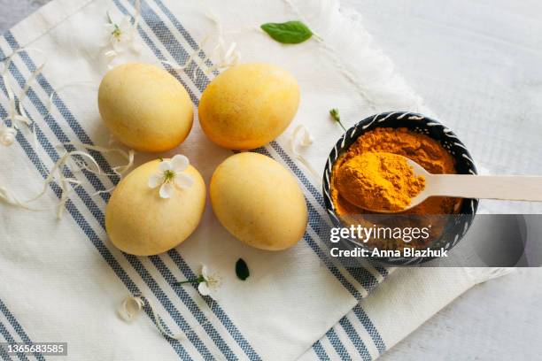 yellow easter eggs over white and blue cotton fabric background and spring cherry blossom. greeting card for holidays. natural dye for eggs made of turmeric powder. - painted easter eggs stock pictures, royalty-free photos & images
