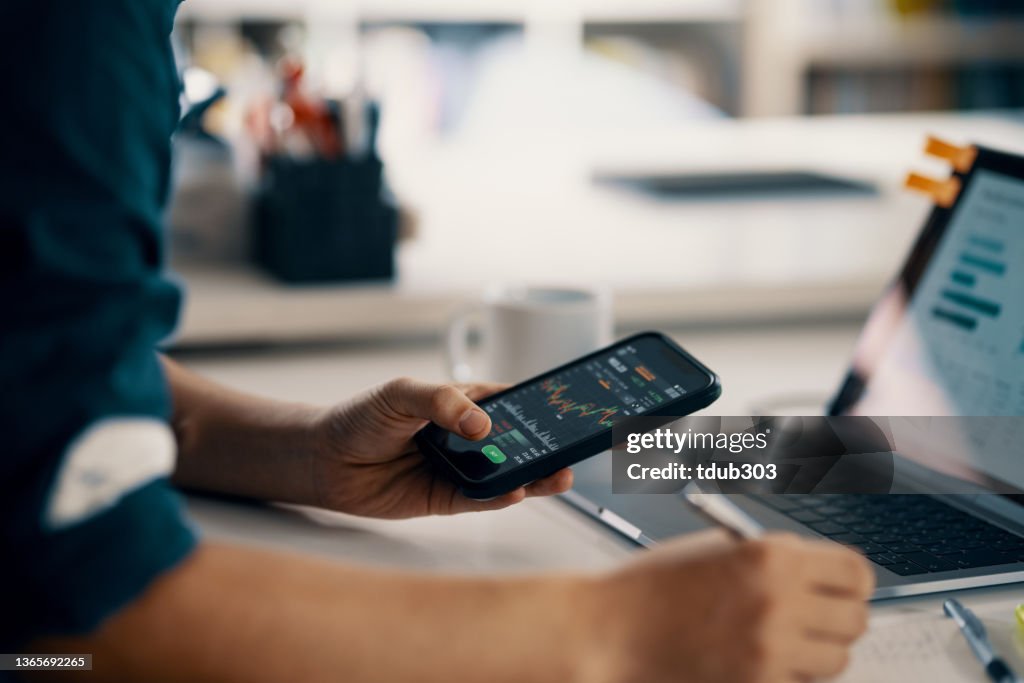 Mittlerer Erwachsener Mann, der Finanzinformationen auf einem Smartphone überprüft, während er seine Buchhaltung führt