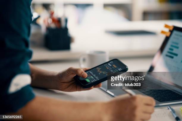 mittlerer erwachsener mann, der finanzinformationen auf einem smartphone überprüft, während er seine buchhaltung führt - aktienkurs stock-fotos und bilder