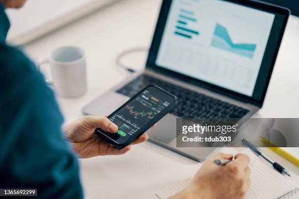 mid adult man checking financial information on a smart phone while doing his bookkeeping - smart numbers office stockfoto's en -beelden