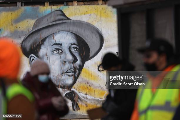 Mural featuring a portrait of civil rights icon Emmett Till looks out from an abandoned building front as volunteers gather nearby with family...