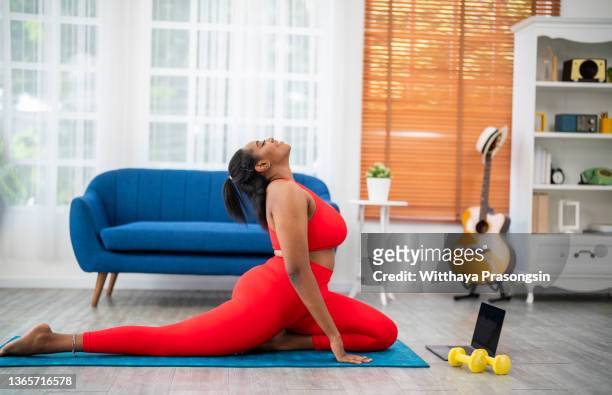 young african curvy woman doing pilates virtual fitness class with laptop at home - sport wellness people lifestyle - curvy black women - fotografias e filmes do acervo