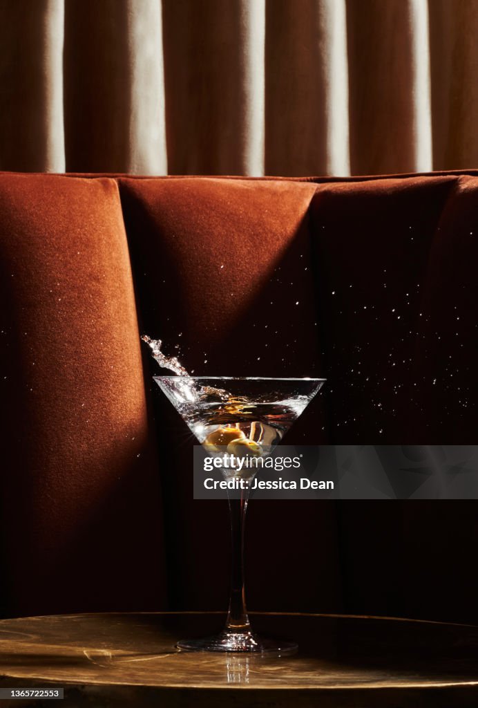 Martini glass with splashing olives in swanky environment.