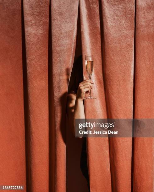 a woman stands behind a velvet curtain toasting with champagne. - glamourous woman stock-fotos und bilder