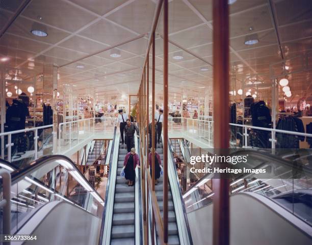 Eldon Square Shopping Centre, Newgate Street, Newcastle upon Tyne, . Two shoppers descending an escalator followed by a security guard in the H&M...