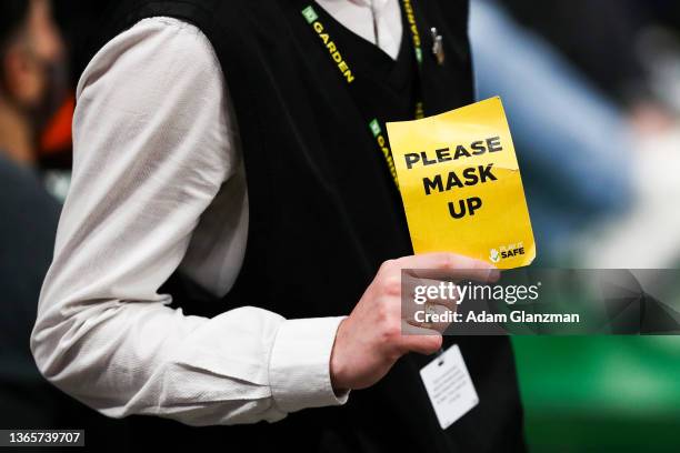 An usher holds a sign encouraging people to put their masks on to protect the crowd from the spread of COVID-19 during a game between the Boston...