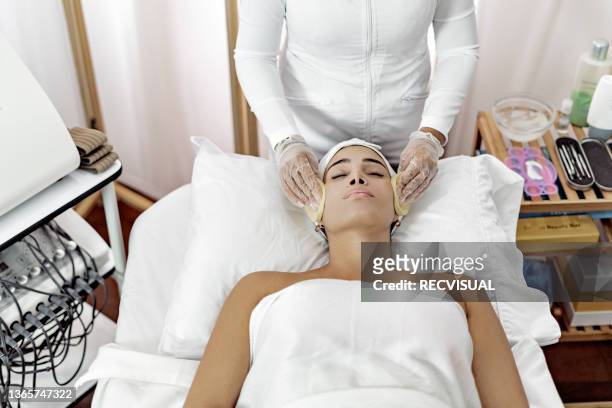 professional beautician cleanses the face of a young woman lying on a massage table - parte del cuerpo humano stock pictures, royalty-free photos & images