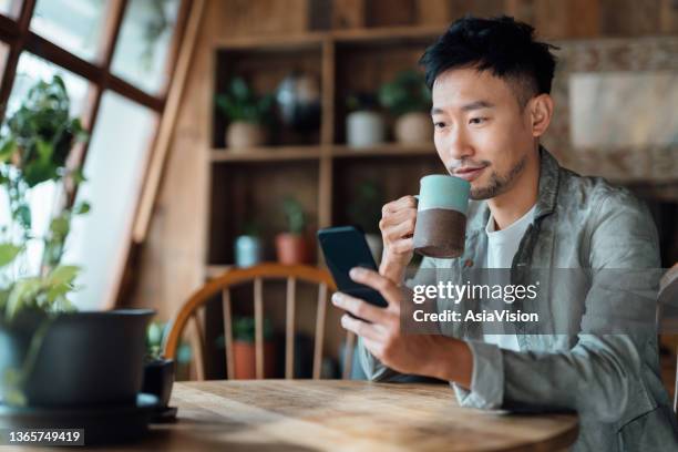 young asian man managing online banking with mobile app on smartphone, taking care of his money and finances while relaxing at home. banking with technology - market intelligence imagens e fotografias de stock