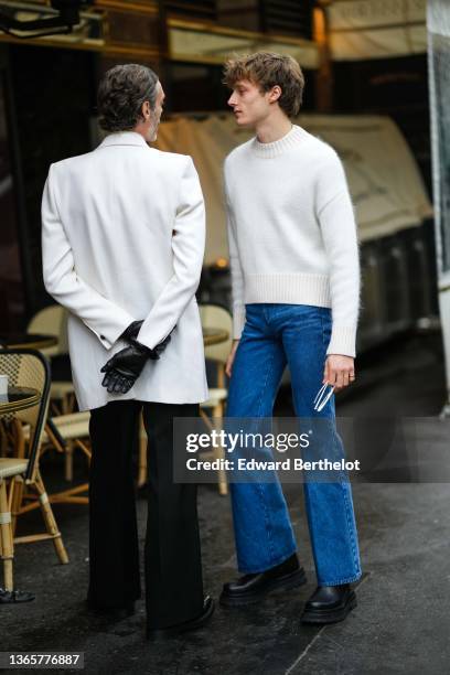 Guest wears a white blazer jacket, black leather gloves, black flared suit pants, black shiny leather shoes, a guest wears a white wool pullover,...