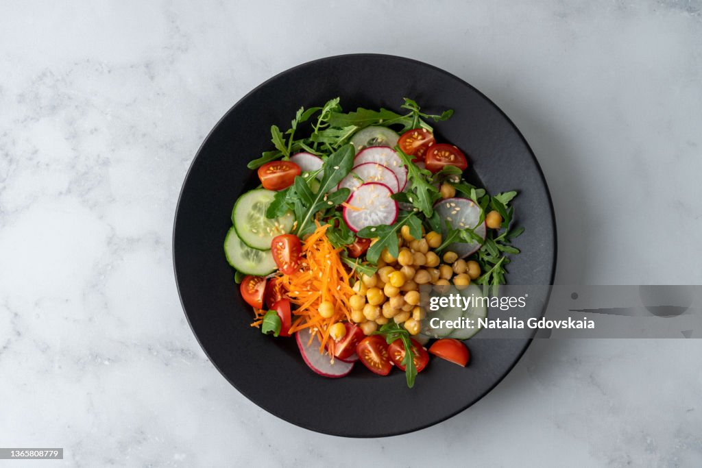 Top view of vegetarian fresh salad with tomatoes, cucumbers, carrots, redishes, aragula, chickpeas