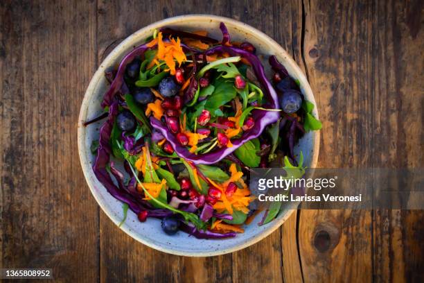 salad with red cabbage, carrots, blue berries, and pomegranate seeds - salad bowl stock pictures, royalty-free photos & images