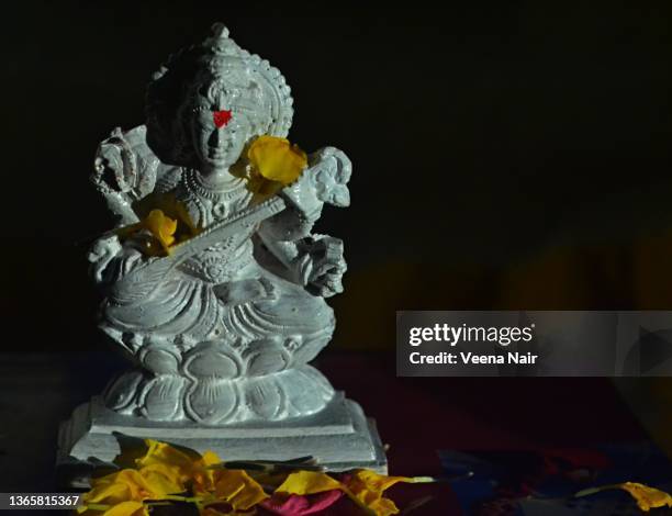 white idol of goddess saraswati on books/ yellow marigold flowers/morning light/vasant panchami/india - saraswati stock-fotos und bilder