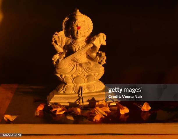 white idol of goddess saraswati on books/ yellow marigold flowers/morning light/vasant panchami/india - saraswati puja stockfoto's en -beelden