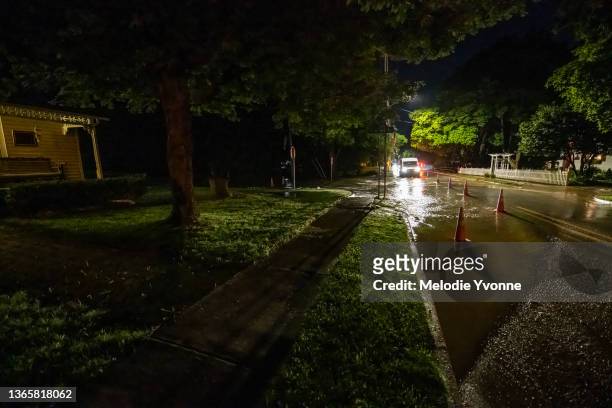 color horizontal wide view of water main break & flood on suburban street at night lit by headlights and streetlights - water main stock-fotos und bilder