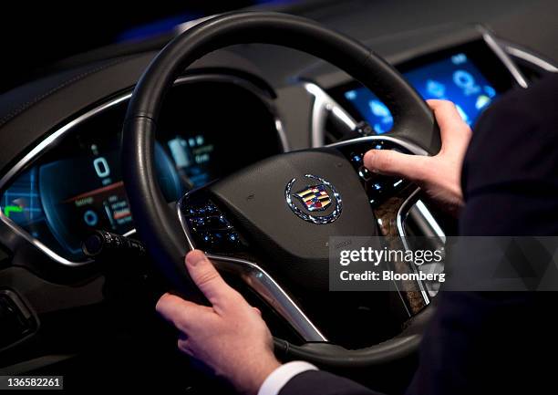 An attendee grips the steering wheel of the General Motors Co. Cadillac User Experience Infotainment model during the unveiling of the 2013 Cadillac...