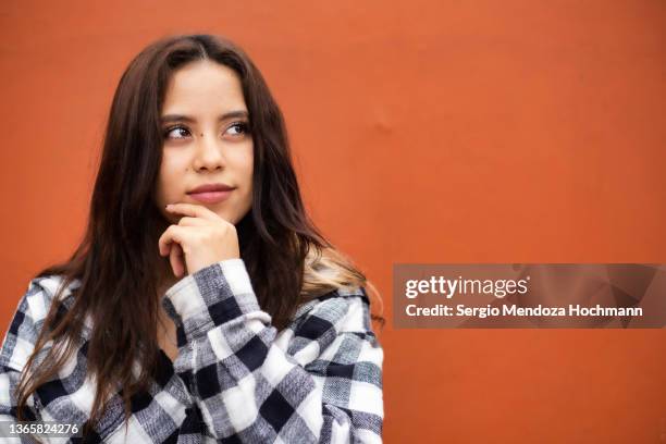 young latino woman deep in thought, thinking with hand on her chin - woman thinking hand on chin stock pictures, royalty-free photos & images