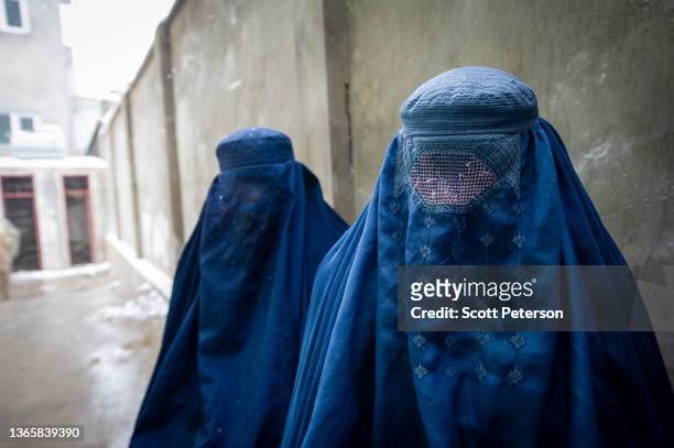 Two women wearing burqas pause for a portrait after having their ration cards checked, as the UN World Food Program distributes a critical monthly...