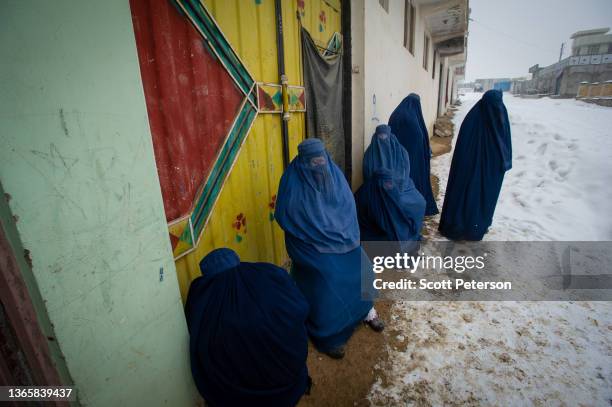 Afghan women wearing burqas line up to have their ration cards checked, as the UN World Food Program distributes a critical monthly food ration, with...