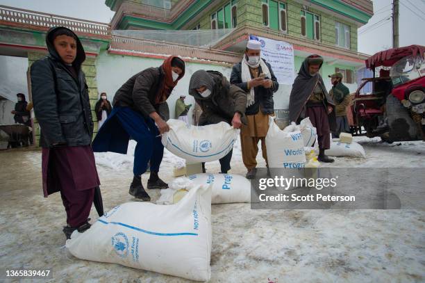 Afghan men prepare to transport sacks of flour, as the UN World Food Program distributes a critical monthly food ration, with food largely supplied...