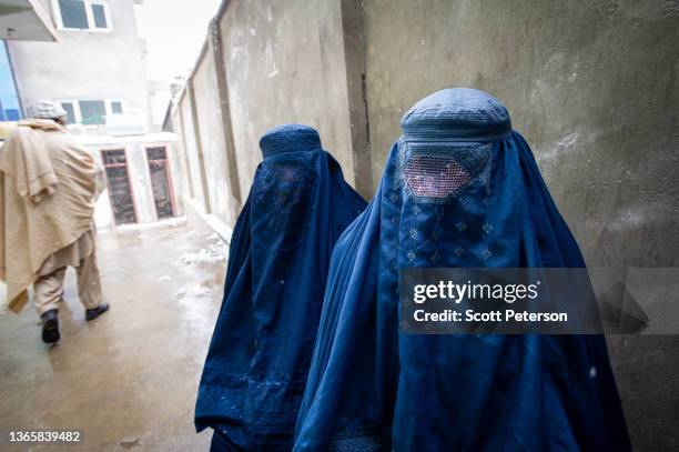 Two women wearing burqas pause for a portrait after having their ration cards checked, as the UN World Food Program distributes a critical monthly...