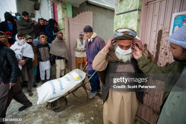 An Afghan man puts on a facemask to prevent the spread of Covid-19, as the UN World Food Program distributes a critical monthly food ration, with...