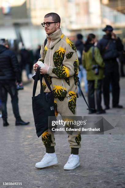 Guest wears glasses, a beige with khaki and yellow print pattern zipper / high neck pullover, matching beige with khaki and yellow print pattern...