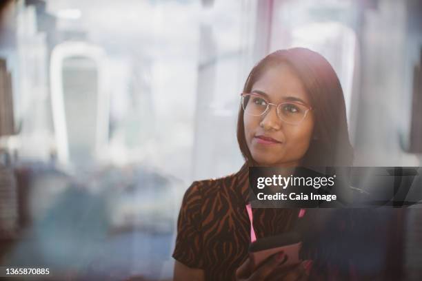 thoughtful businesswoman with smart phone in sunny window - looking away stock pictures, royalty-free photos & images