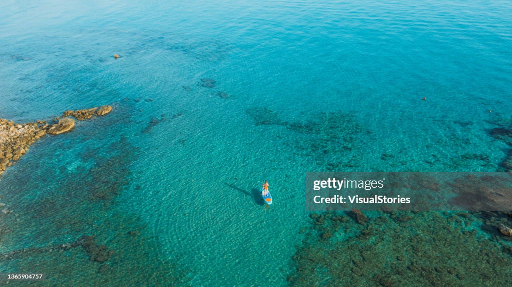 Aerial view of female paddleboarding in the turquoise sea on Zakynthos island, Greece