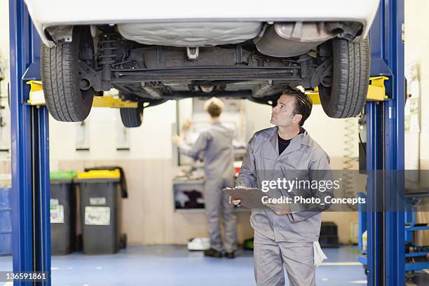 mechanic examining underside of car - auto garage stockfoto's en -beelden