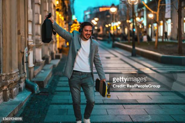 young businessman with skateboard listening to music - city to surf stock pictures, royalty-free photos & images